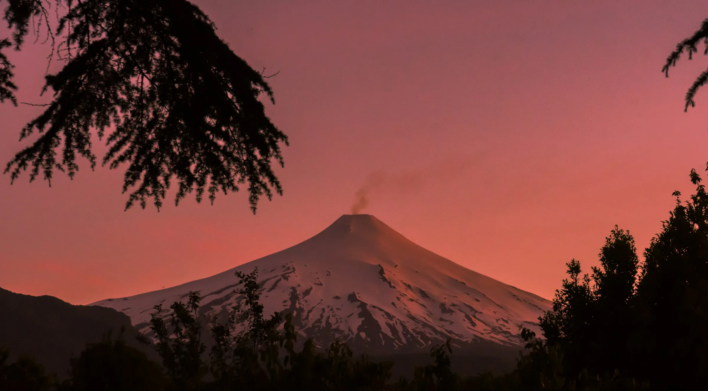 Snow-covered Villarrica volcano glowing beneath an intense red evening sky above Pucón